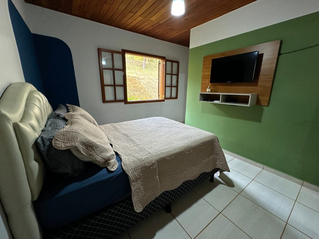 Suíte Jequitibá — quarto com parede verde e TV
